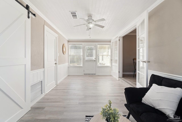 interior space with ornamental molding, a barn door, light wood-type flooring, and ceiling fan