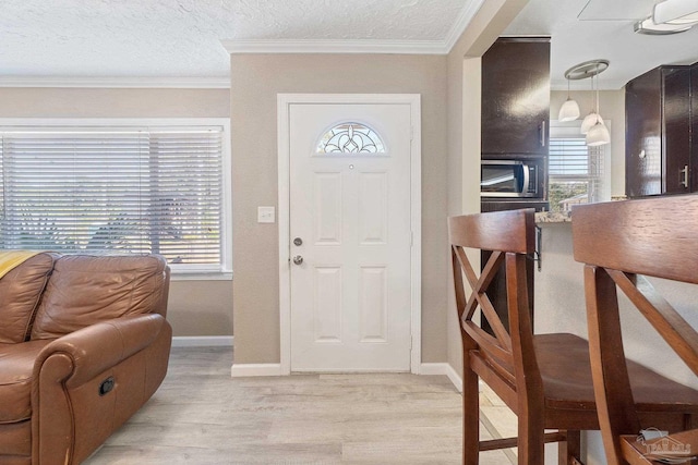 foyer entrance featuring a textured ceiling, ornamental molding, a wealth of natural light, and light wood-type flooring