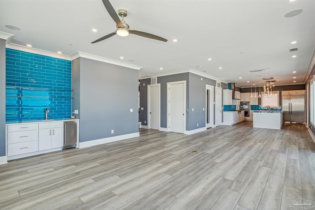 unfurnished living room with sink, ornamental molding, ceiling fan, and light wood-type flooring