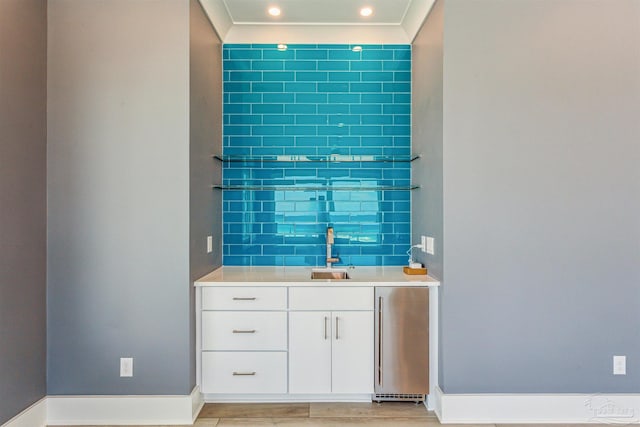 bar featuring white cabinetry, sink, high end refrigerator, decorative backsplash, and light wood-type flooring