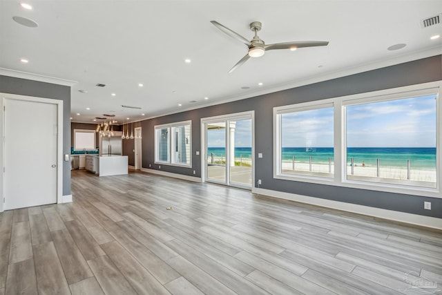 unfurnished living room with a water view, ornamental molding, a view of the beach, and light wood-type flooring