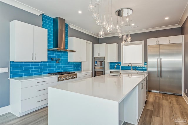 kitchen with white cabinets, stainless steel appliances, an island with sink, and wall chimney range hood