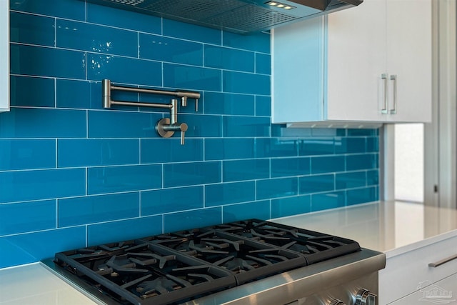 kitchen featuring gas range, white cabinetry, decorative backsplash, and wall chimney range hood