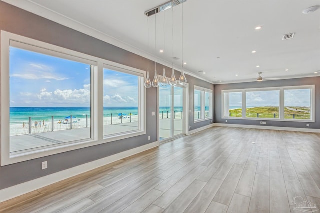 unfurnished living room featuring ornamental molding, a beach view, and a water view