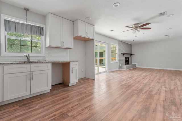 kitchen with pendant lighting, a brick fireplace, light hardwood / wood-style flooring, and white cabinetry