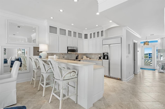 kitchen with white cabinetry, crown molding, paneled built in fridge, kitchen peninsula, and backsplash