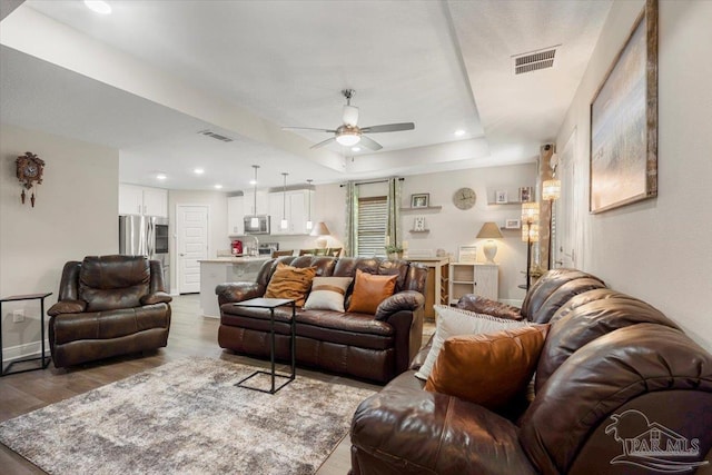 living room featuring hardwood / wood-style flooring, ceiling fan, and a raised ceiling