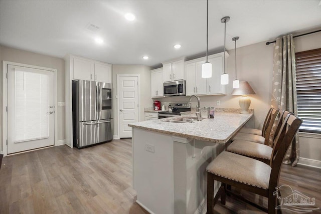 kitchen featuring white cabinetry, kitchen peninsula, pendant lighting, stainless steel appliances, and light stone countertops