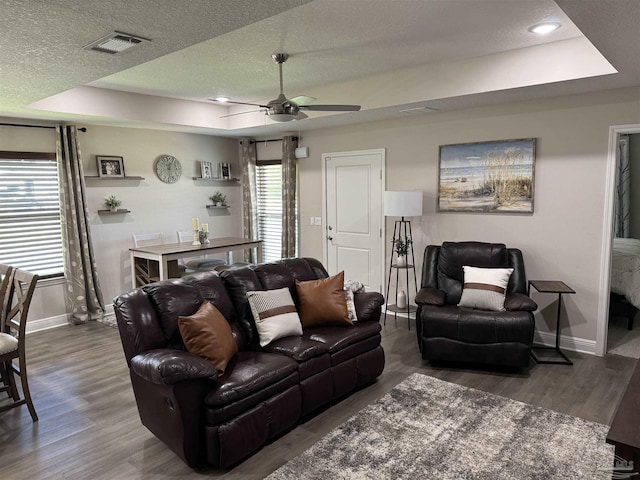 living room with ceiling fan, a tray ceiling, dark hardwood / wood-style floors, and a textured ceiling