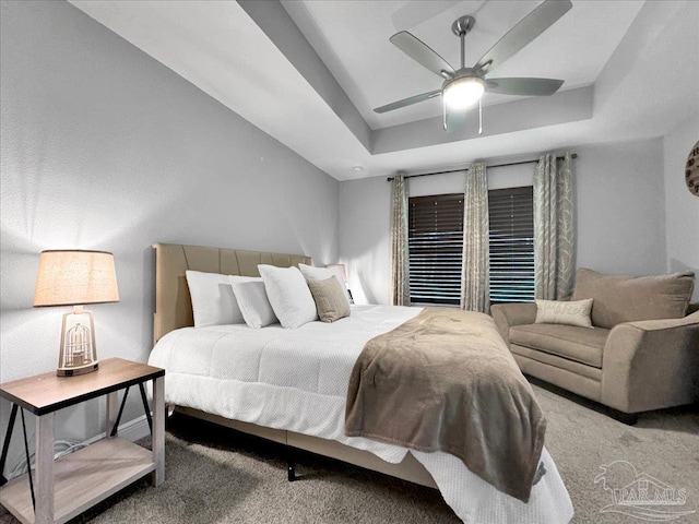 carpeted bedroom with a raised ceiling and ceiling fan