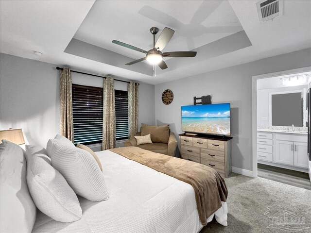 bedroom featuring ensuite bathroom, sink, ceiling fan, and a tray ceiling