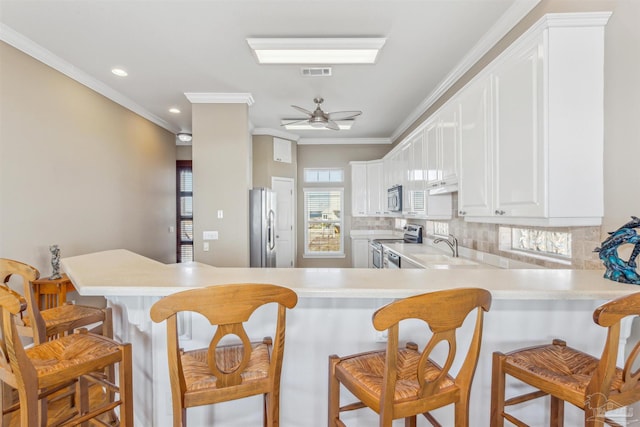 kitchen featuring kitchen peninsula, a kitchen breakfast bar, ornamental molding, stainless steel appliances, and sink