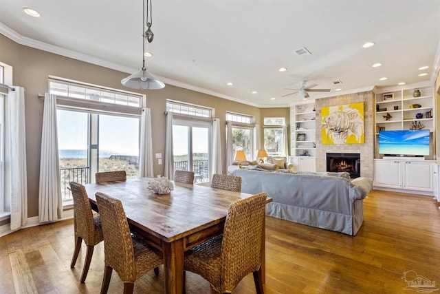 dining area with crown molding, a fireplace, ceiling fan, and light hardwood / wood-style floors