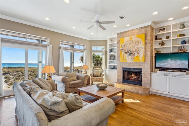 living room with a fireplace, a water view, ceiling fan, and ornamental molding