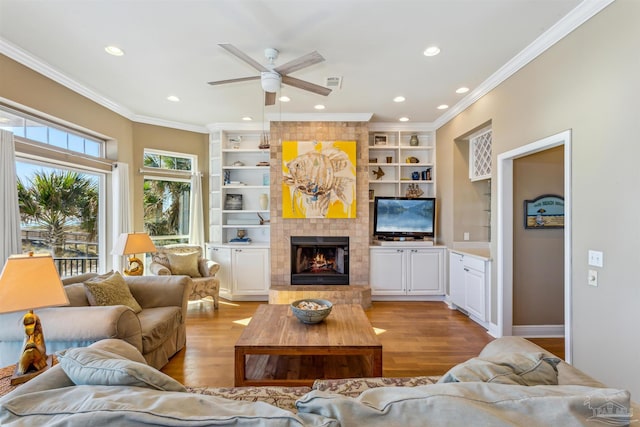 living room with light hardwood / wood-style floors, ceiling fan, ornamental molding, and a tiled fireplace