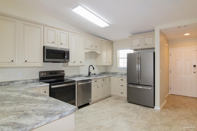 7101 Joy St Unit J5, Pensacola, FL 32504 - kitchen with stainless steel appliances, cream cabinetry, vaulted ceiling, a sink, and light stone counters