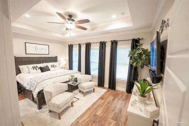 bedroom with ornamental molding, ceiling fan, light hardwood / wood-style floors, and a tray ceiling