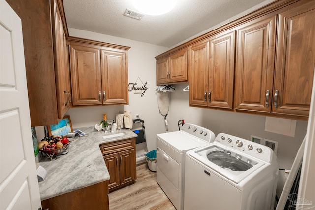 clothes washing area featuring sink, cabinets, separate washer and dryer, light hardwood / wood-style flooring, and a textured ceiling