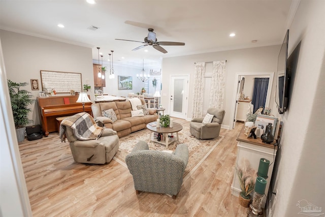 living room with ceiling fan with notable chandelier, ornamental molding, and light hardwood / wood-style floors