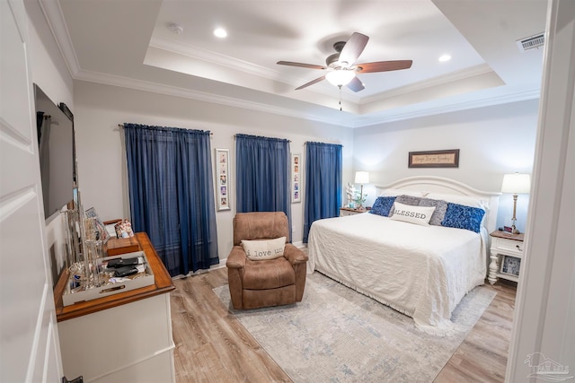 bedroom with crown molding, a tray ceiling, ceiling fan, and light wood-type flooring