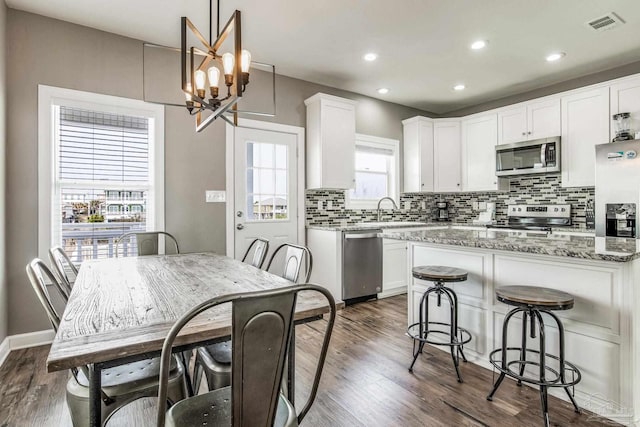 kitchen featuring white cabinetry, dark stone countertops, stainless steel appliances, decorative backsplash, and decorative light fixtures