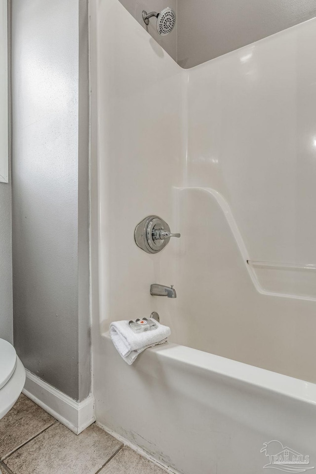 bathroom with washtub / shower combination, toilet, and tile patterned flooring