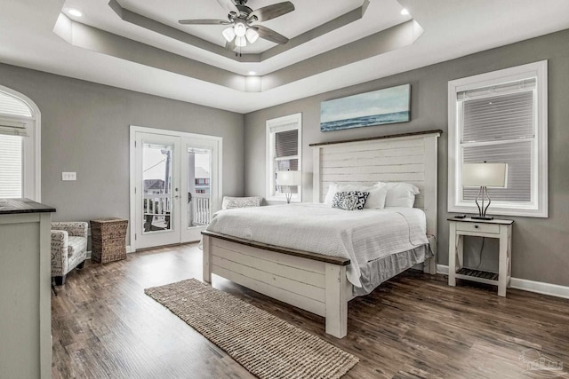 bedroom with ceiling fan, a tray ceiling, dark hardwood / wood-style flooring, and access to outside