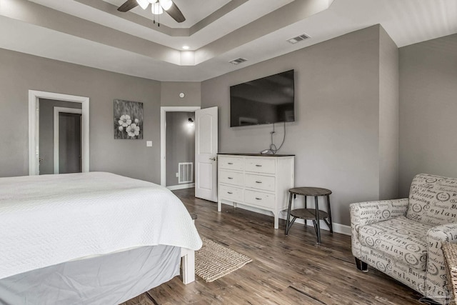 bedroom with dark hardwood / wood-style floors, ceiling fan, and a tray ceiling