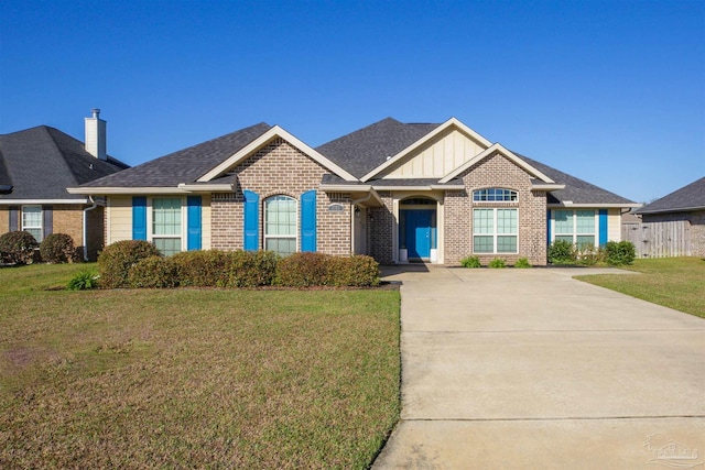 view of front of home featuring a front yard, fence, roof with shingles, brick siding, and board and batten siding