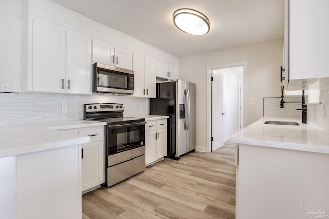 kitchen with stainless steel appliances, white cabinets, a sink, and light wood-style flooring