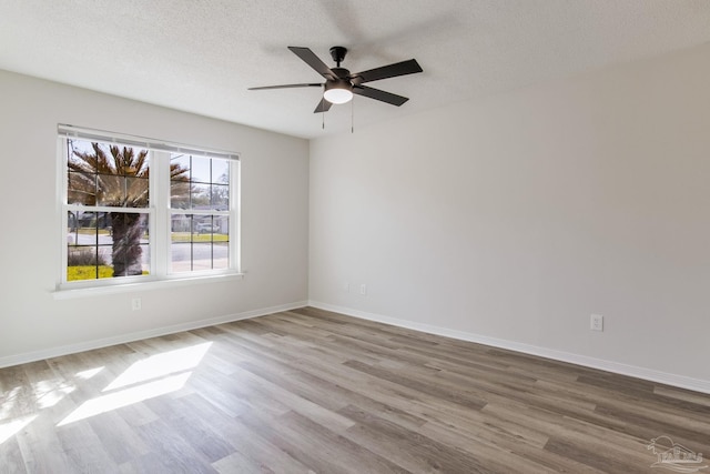 empty room featuring a textured ceiling, wood finished floors, and baseboards