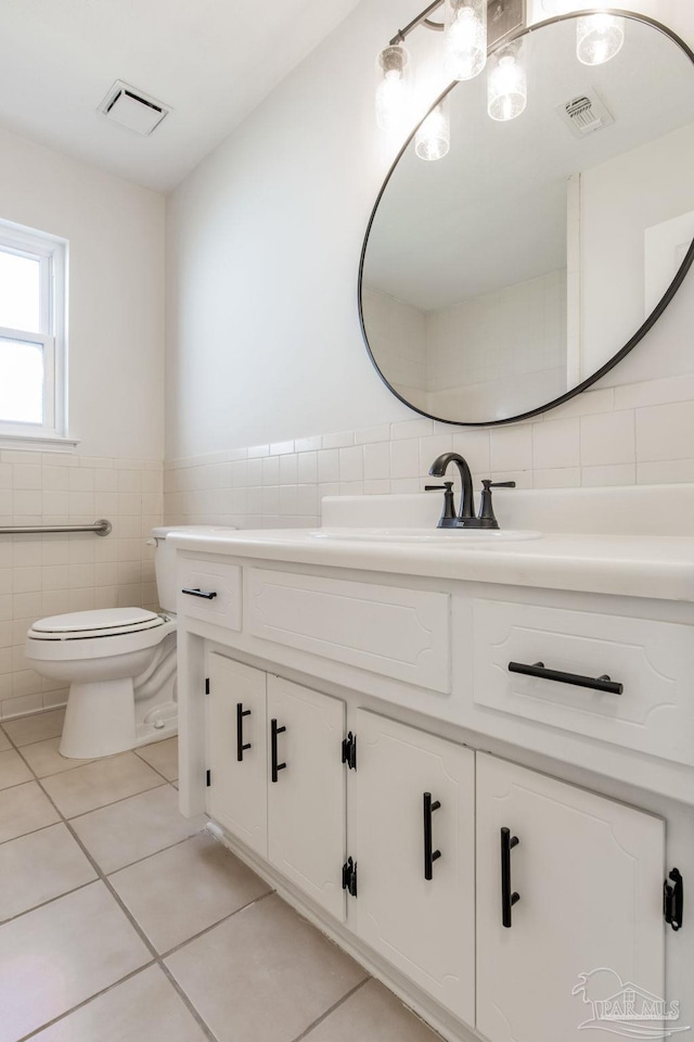 bathroom featuring visible vents, toilet, tile patterned floors, vanity, and tile walls