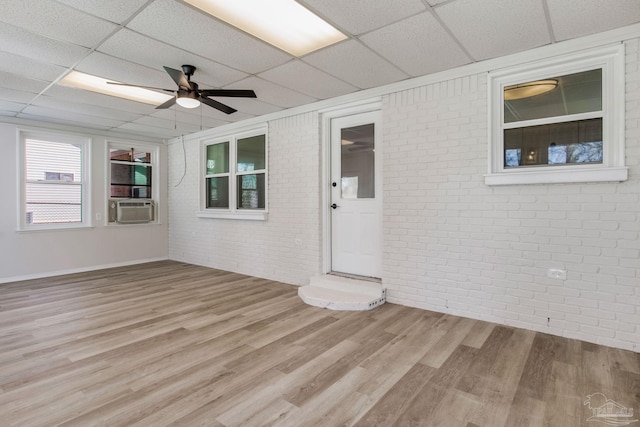 interior space featuring a ceiling fan, a paneled ceiling, light wood-style flooring, and brick wall