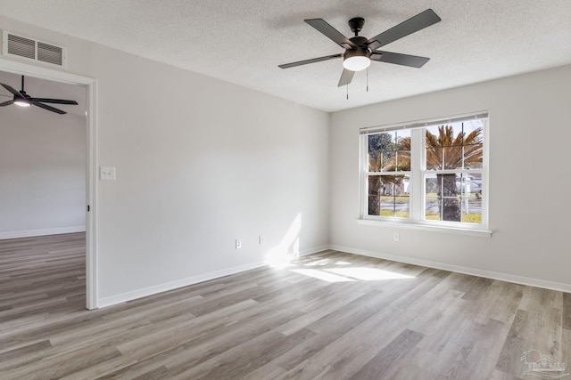 empty room with a textured ceiling, wood finished floors, visible vents, and baseboards