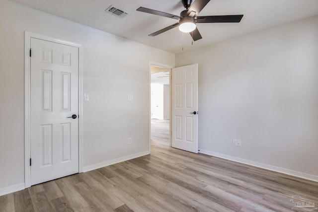 unfurnished bedroom featuring light wood-type flooring, visible vents, a textured ceiling, and baseboards