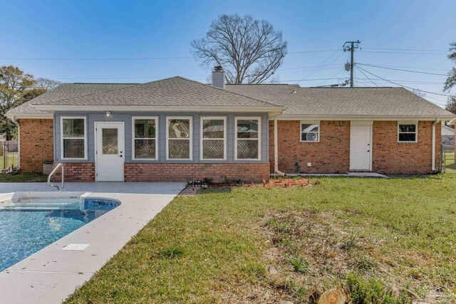 back of property featuring brick siding, roof with shingles, a chimney, and a yard