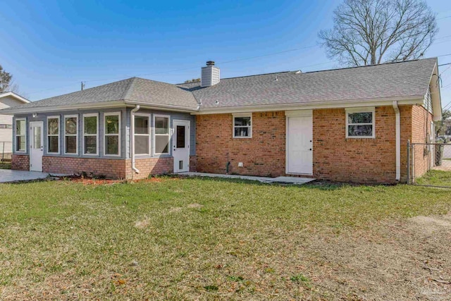 back of house with a yard, brick siding, a chimney, and a shingled roof