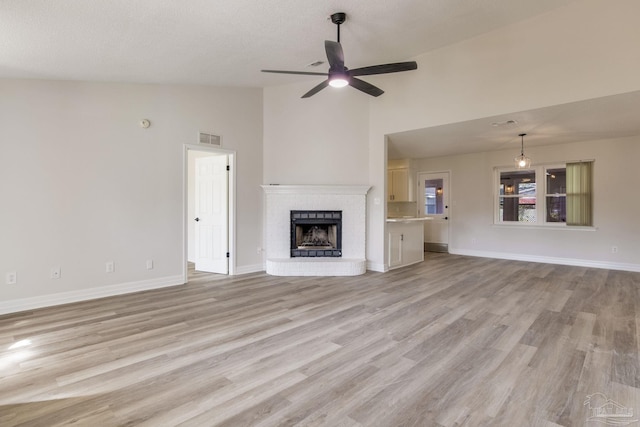 unfurnished living room featuring lofted ceiling, a brick fireplace, visible vents, and light wood finished floors