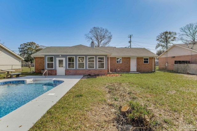 rear view of house featuring a fenced in pool, brick siding, a chimney, a lawn, and fence