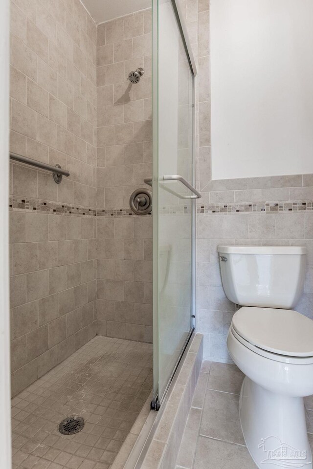 full bath featuring tile walls, tile patterned flooring, a shower stall, and toilet