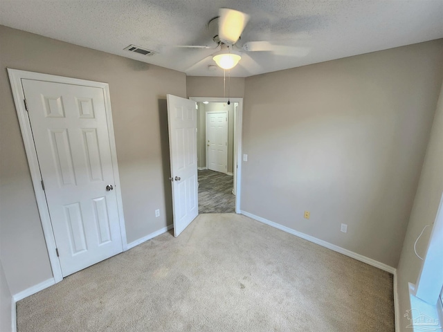 unfurnished bedroom featuring a textured ceiling, carpet, visible vents, and baseboards