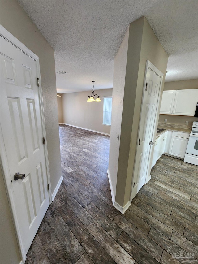 hall with a textured ceiling, a notable chandelier, a sink, baseboards, and dark wood-style floors