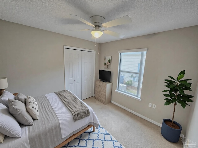 bedroom featuring ceiling fan, a textured ceiling, light colored carpet, baseboards, and a closet