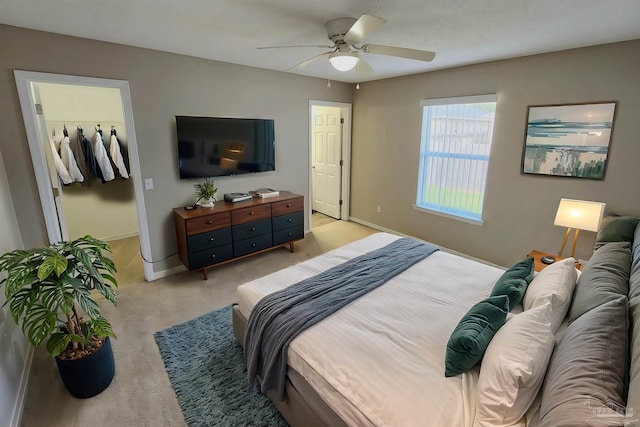 bedroom with light carpet, a spacious closet, a ceiling fan, and baseboards