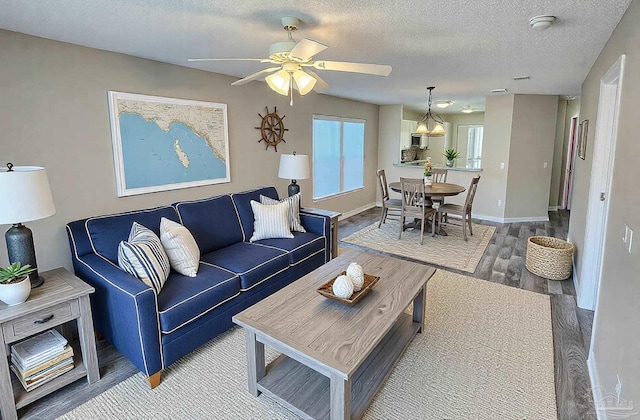 living area with a ceiling fan, a textured ceiling, baseboards, and wood finished floors