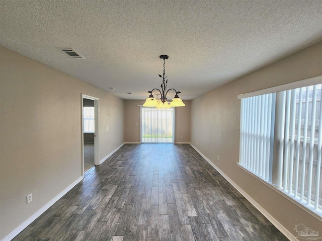 unfurnished dining area with a textured ceiling, a notable chandelier, visible vents, baseboards, and dark wood-style floors