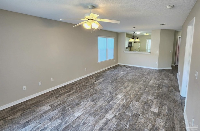 empty room with a textured ceiling, ceiling fan, dark wood finished floors, and baseboards