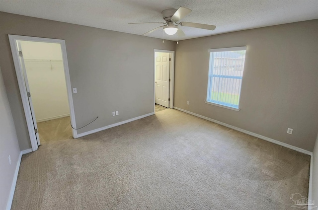 unfurnished bedroom featuring light colored carpet, a spacious closet, a ceiling fan, a textured ceiling, and baseboards