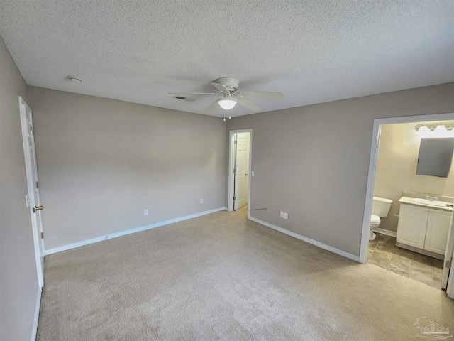 unfurnished bedroom featuring baseboards, connected bathroom, light colored carpet, a textured ceiling, and a sink