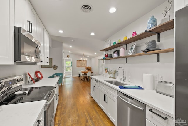 kitchen with appliances with stainless steel finishes, vaulted ceiling, dark wood-type flooring, sink, and white cabinets